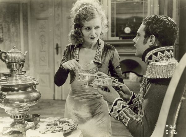 A woman and man in elaborate costumes have tea in the film "Congress Dances".