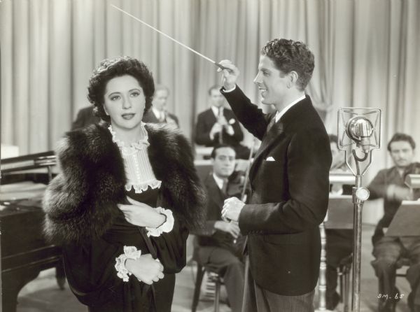Rudy Vallee conducts musicians as a woman sings in "Glorifying the American Girl," a Paramount musical from 1929.
