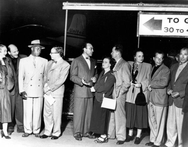 Some members of the Hollywood Ten at an airport. The bald man on the far left is Alvah Bessie. Near the center with his hand gesturing is Herbert Biberman. At the far right is Lester Cole.