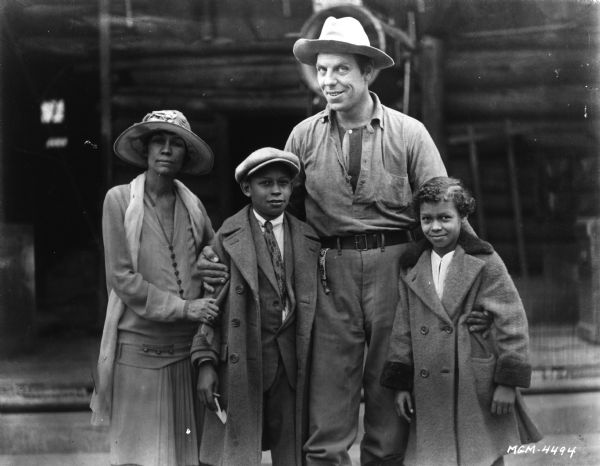 Publicity still of Karl Dane in western wear posing with an African-American woman and her two children.