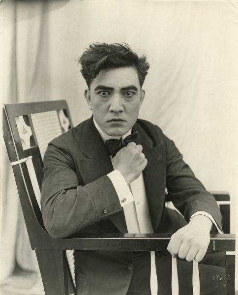 Sessue Hayakawa sits in a chair with his fist raised in a publicity still for "His Birthright" (Haworth 1918).