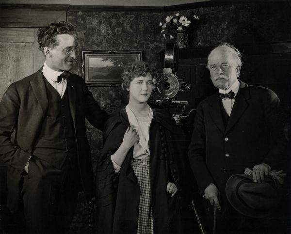 On the set of "The Road to Divorce" (Universal, 1920). Original caption: "Mr. Harry Nuttall, of England, member of the British Parliament from Manchester, visits Universal City while on a tour of America, and is photographed with Mary MacLaren, popular Universal star and her director, Philip Rosen, on a set from 'The Road to Divorce'." Behind them is a Bell & Howell model 2709 camera fitted with an iris diaphragm.