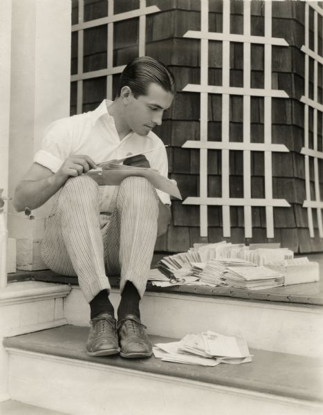 Original caption:
"Does Dick Barthelmess read 'fan' letters? We'll say he does. The photographer caught him on his porch opening his mail, while waiting for the call to breakfast."