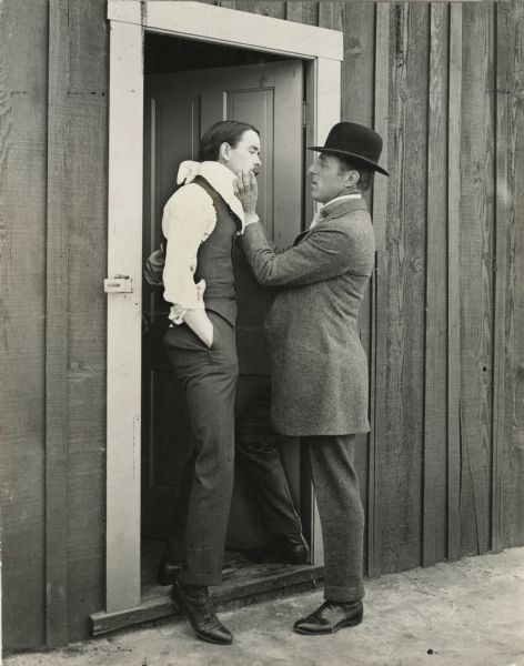 Director D.W. Griffith appears to be adjusting actor Robert Harron's moustache.<p>Original caption: "Making up Bobbie."