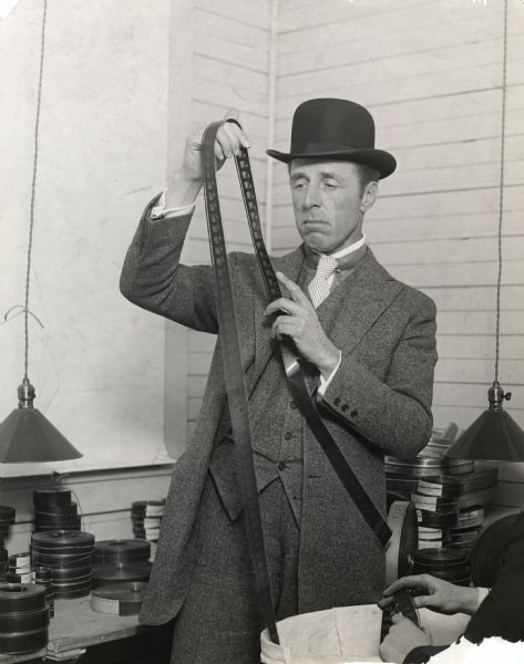 Production still of D. W. Griffith in the editing room examining a piece of film. Original caption: "Mr. Griffith and his cutter at work on <i>Hearts of the World</i>.
