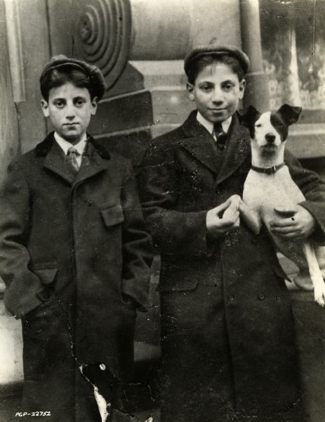 Gummo (Milton Marx) on the left and on the right Groucho (Julius Henry Marx) holding a rat terrier dog.

Caption from Paramount Pictures, Inc.:
"THE BOY GROUCHO--at sixteen, Groucho Marx was a seasoned vaudeville performer. He was the only member of the later famed Four Marx Brothers to be on the stage at that time."
