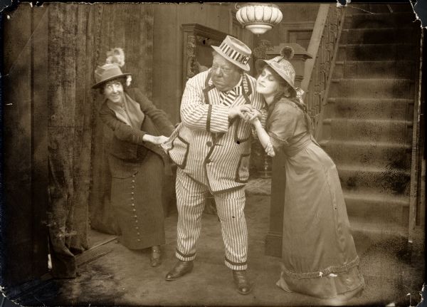 Scene still from the Vitagraph production <i>Father's Flirtation</i>. From left to right are Flora Finch, John Bunny, and Mary Anderson. Bunny wears a boldly striped suit and hat.