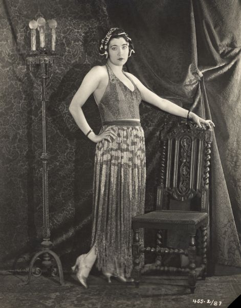 Full-length portrait of Nita Naldi standing by a Spanish-style chair. The photograph was probably made by Donald Biddle Keyes as publicity for the 1922 Paramount feature <i>Blood and Sand.</i>