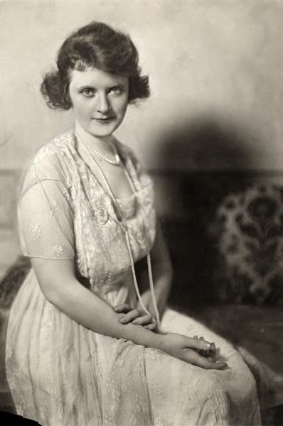 Three-quarter length seated portrait of Billie Burke distributed as publicity for the 1918 Famous Players-Lasky film comedy <i>The Make Believe Wife</i>. The photograph was retouched for newspaper use.