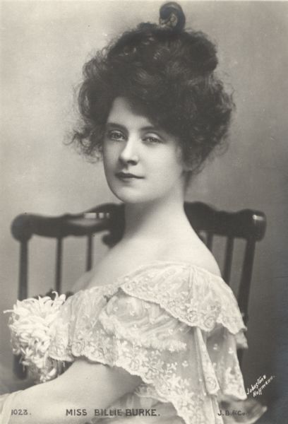 Johnston & Hoffmann publicity photograph of Billie Burke in a lacy dress with her hair piled on top of her head. Reproduced as a postcard by J. Beagles & Company of London, England.