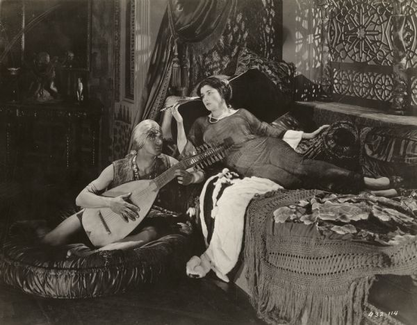 Doña Sol de Guevara (played by Nita Naldi) relaxes smoking a cigarette on a divan as her male servant plays the lute in the 1922 Famous Players-Lasky production <i>Blood and Sand.</i>