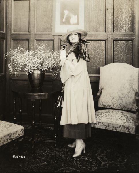 Full-length publicity portrait of Lenore Ulric wearing fashionable cool weather clothes and clutching an umbrella with an extremely long handle.