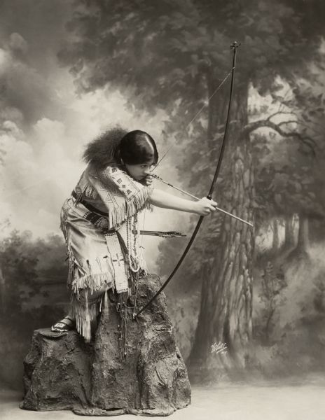Lenore Ulric draws her bow crouched on a papier-mâché boulder. She starred as Wetona in the 1916 Frohman-Belasco Broadway production <i>The Heart of Wetona</i> which opened at the Lyceum Theatre in February 1916.
