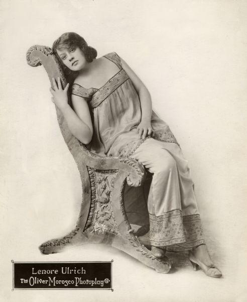 Full-length publicity portrait of Lenore Ulric lounging on a medieval-looking chair.
