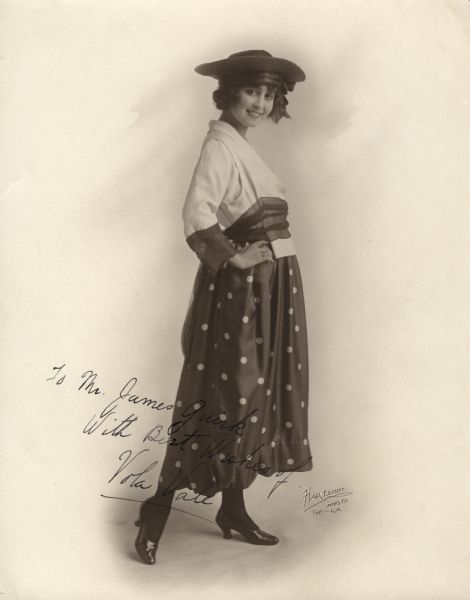 Silent film actress Vola Vale wearing a polka dot dress and dark straw hat in a portrait by the Hartsook Studio. She inscribed it to the editor and publisher of <i>Photoplay</i> magazine:
"To Mr. James Quirk, with best wishes of Vola Vale."