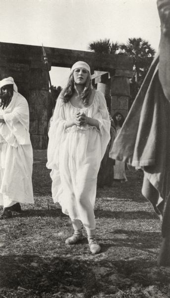 Valda Valkyrien wears a flowing white robe, probably in the role of Ashubetis on the Jacksonville, Florida, set of the 1917 Thanhouser production <i>The Image Maker</i>.  The original caption: "This is where those nasty Egyptian soldiers have captured Valkyrien and are leading her off to the crocodile pit. Please note death agony in her face, and the beautiful classic silhouette of her garments. Also, she is not going to dine on the crocodiles but they on her. She is fond of lobsters as a beast of prey to be fondly devoured but she can live without the saurians."
