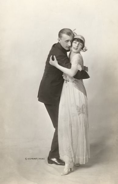 Full-length portrait of the celebrated dancing partners Vernon and Irene Castle dancing cheek to cheek. Irene wears a gauzy dress decorated with butterflies.