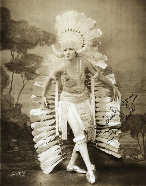 Full-length studio portrait of the dancer Irene Castle in an American Indian costume with many feathers. It is autographed "Sincerely Yours, Irene Castle."