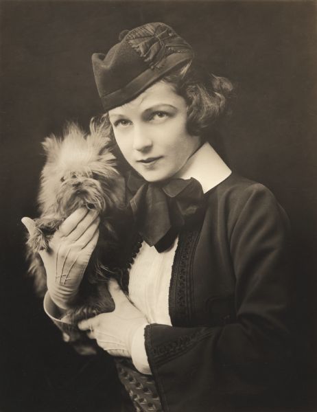 Waist-up portrait of Irene Castle holding one of her small Belgian Griffon dogs.