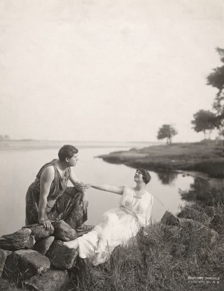 The French operatic tenor Lucien Muratore and his wife, the Italian soprano, Lina Cavalieri. They are costumed in classical style and lounging by Long Island Sound.

Original  caption:
"Lucien Muratore and Lina Cavalieri at their summer home at Waterford, Conn. Lina is training for her Paramount engagement and Lucien for his opera season. March 1919."