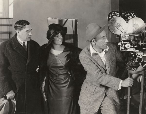 The opera stars Lucian Muratire, French tenor, and his wife Lina Cavalieri, Italian soprano, visit film director William de Mille who is posed with a Bell and Howell camera. Cavaliere acted in silent films for Famous Players-Lasky from 1917 to 1919.