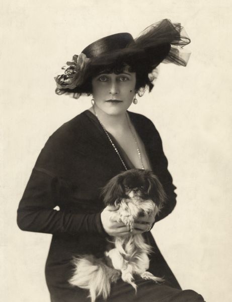 Seated portrait of Kitty Gordon holding a Pekingese dog in her lap and wearing a black straw hat. It was used as publicity for her April 1913 vaudeville appearance at Keith's Colonial in New York.