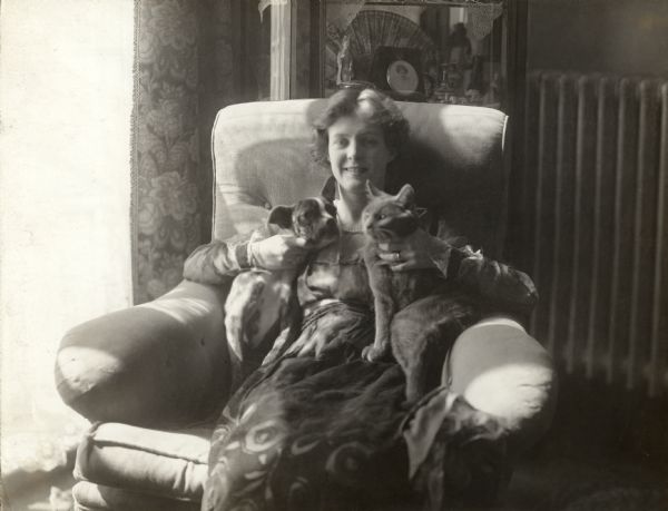 Taliaferro sits in an overstuffed chair and holds her pets still for the photographer.

Original caption:
"Mabel Taliaferro, Metro Star, in the library of her New York apartment with her pets 'Hopey' and 'Gertie.'"