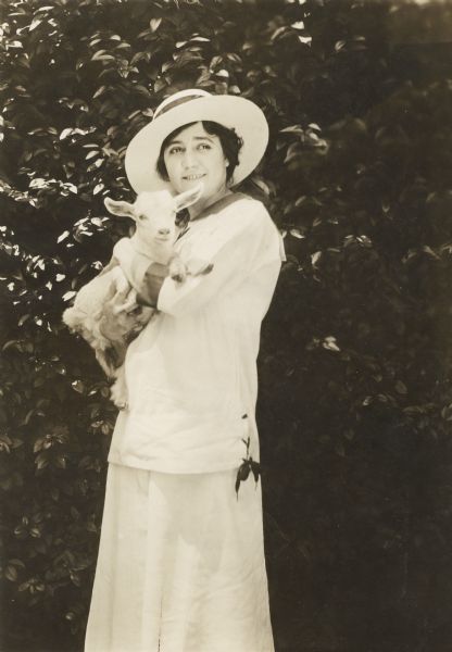 Mabel Trunnelle, player in Edison Company silent films from 1909, is dressed in a white sailor's suit and straw hat and holds a young goat.