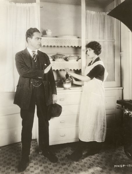 Marshall Neilan, the director of <i>Don't Ever Marry</i> (1920), and Marjorie Daw, the female lead.
Original caption:
"NIX ON THE FANCY FOOD, SAYS MARSHALL NEILAN.
Marjorie Daw, leading lady in <i>Don't Ever Marry</i> has a weakness for trying new recipes whenever she has a few hours to spare at the studio. In the Neilan studio, adjoining her dressing room, is a little kitchen in which her meals-at-the-studio are cooked. Also it is the place where Marjorie tries her new stunts in cookery on the property boys, grips and any others who happen to have enough nerve to take a chance. Here we have a close-up of Marshall Neilan himself trying to persuade Marjorie to stop before she kills off the entire technical staff of Marshall Neilan Productions."