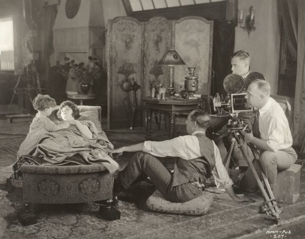 Production still from <i>All Souls' Eve</i>, a Realart silent film released in 1921. Seated  on a cushion on the floor, Chester Franklin is directing a tender scene with the child actor Mickey Moore (Michael D. Moore) and Mary Miles Minter. Behind Franklin are the cameraman Faxon Dean (probably in the white striped shirt) and his assistant operating a Bell and Howell model 2709 camera.