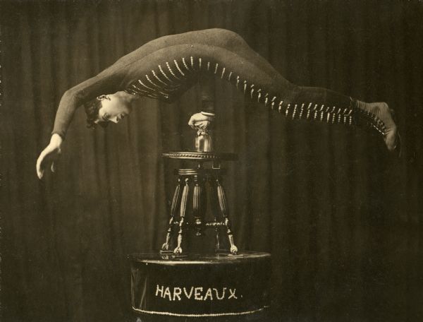 Allie Harveaux, an acrobat, in a promotional photograph for his balancing act. His body is parallel to the floor supported only by his right hand which is balanced on a beer glass on top of a piano stool on top of a table trimmed with a cloth on which the name HARVEAUX is spelled in buttons.

Harveaux was from Washburn County Wisconsin and toured on the Sullivan-Considine and Orpheum vaudeville circuits from c. 1907 to 1912 as the "Boneless Wonder."