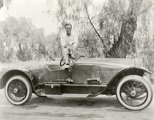 Silent film star Douglas Fairbanks stands in the cockpit of a Stutz Bearcat roadster.