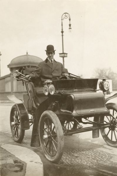 Comic actor Fred Stone holding the tiller of an early two-seat runabout. The automobile may be a Woods Electric or Woods Dual Power. Stone had been a circus performer and vaudevillian before he became famous as the Scarecrow in the 1903 Broadway musical <i>The Wizard of Oz.</i>