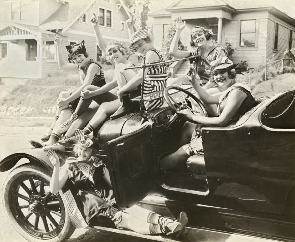 Six Mack Sennett bathing beauties wave as they sit on a Willys Six seven-seat touring car. Three of the actresses are tentatively identified as Marie Prevost (farthest to the left on the car's hood), Peggy Pearce (later known as Viola Barry, directly behind Prevost), and Vera Steadman (in stripes).