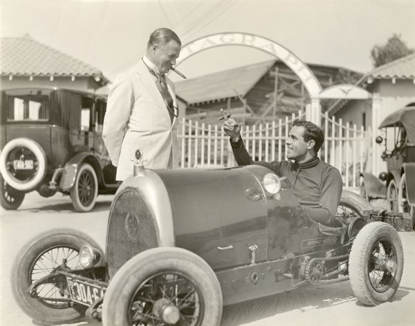 Albert E. Smith, one of the founders of the Vitagraph motion picture company, stands with a cigar in his mouth looking down at the silent film star Antonio Moreno (also with cigar) sitting at the wheel of a small racing car just outside the Vitagraph studio gates in East Hollywood, California. The miniature automobile is an Al Smith Special with 1920 California license plates, no doubt the same car mentioned in the advertisement below:

ACTORS' FUND FESTIVAL
"Five mile auto race between Tony Moreno in Art Smith baby racer and Tod Sloan driving the Stagg-Packard Special."
<i>Los Angeles Times,</i> 3 June 1921, p. II 10.
