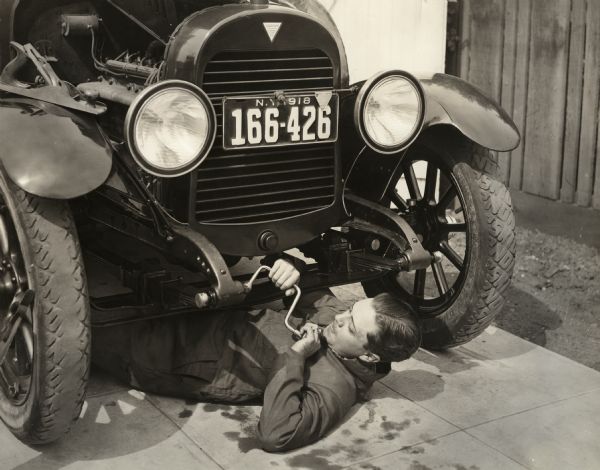 Silent film actor Niles Welch on the ground underneath the front of a 1918 Hudson Super Six touring limousine. Apparently he is using a carpenter's brace drill on the suspension.

Original caption:
"What Niles will do to that Auto will be plenty."