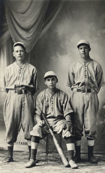 Studio portrait of three young men of the Cross Plains baseball team in front of a painted backdrop. From left to right: Peter Berg, Ray Gorman, and Ernie Dolfen.
