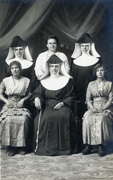 Studio portrait of the Bollenbeck sisters, three of whom were nuns, in front of a painted backdrop. First row from left to right: Mary Haack, Sister Claudia, and Anna Bowar. Second row from left to right: Sister Polycarp, Julia Bollenbeck, and Sister Sylvia.