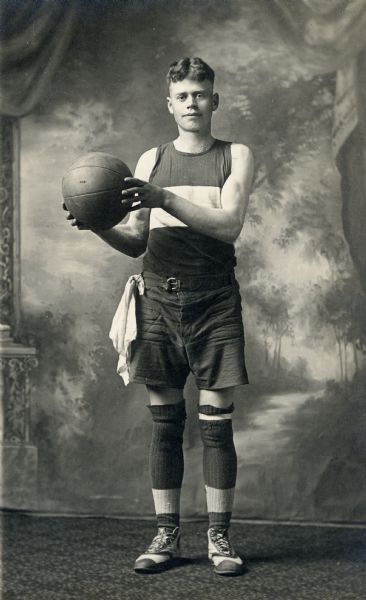 Studio portrait in front of a painted backdrop of Rudolph Faust holding up a basketball.