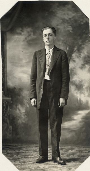 Full-length studio portrait of Jake Esser dressed in a suit and tie standing in front of a painted backdrop.