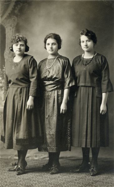 Studio portrait of, from left to right, Mary Brunner Muskat, Ida Brunner Muskat and Laura Brunner Zander standing in front of a painted backdrop.