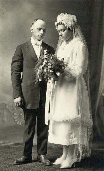 Wedding studio portrait of Mr. and Mrs. Leo Haak posing in front of a painted backdrop.