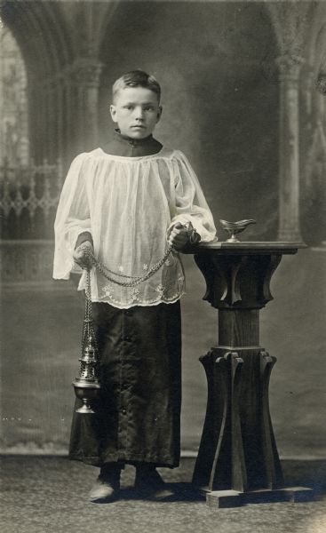 Studio portrait in front of a painted backdrop of Raymond Bowar dressed in his altar boy robe and holding an incense burner.
