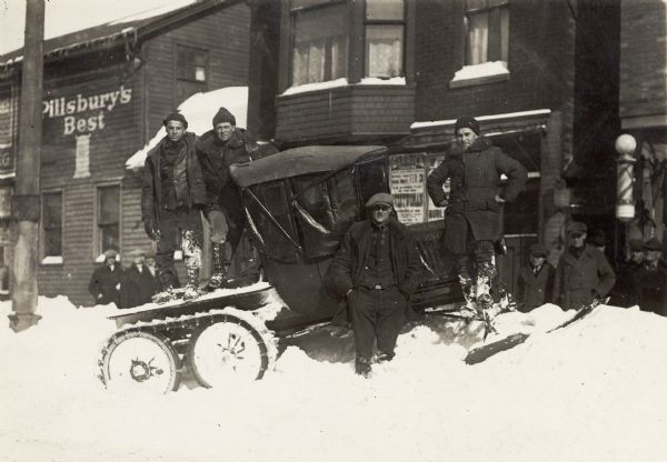 Winter scene with Harold O. Hornburg of Hartland, Wisconsin, who stated that "he is standing on the front of the machine with his hands on his hips. His buddy, Allen D. Wilde (behind with his arm resting on the top of the machine), also from Hartland, and another unidentified friend, made this vehicle as a recreational venture from a Model T Ford chassis (like an early snowmobile), and attempted to get to Milwaukee during a heavy snowfall. They did."<p>Described in an ad from the Mission House (now Lakeland College Spectrum), 1929, as The Snow Flyer, made by The Snow Flyer Corp., New Holstein, Wisconsin.</p>