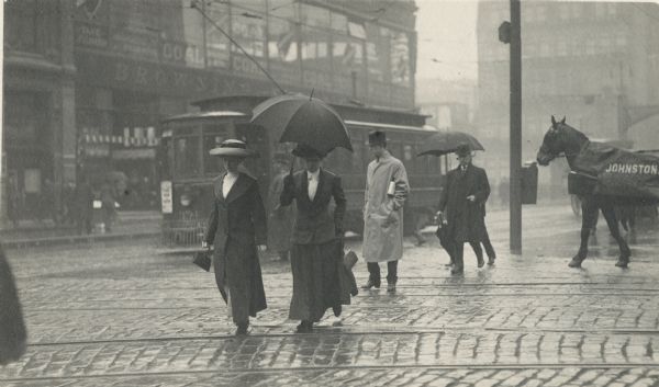 Several pedestrians cross a city street on a rainy day.