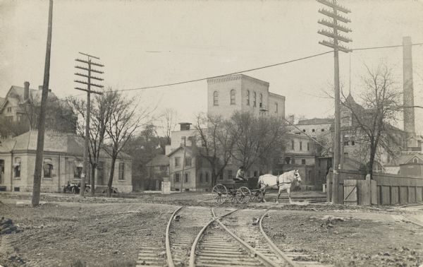 A man in a horse-drawn vehicle crosses railroad tracks.
