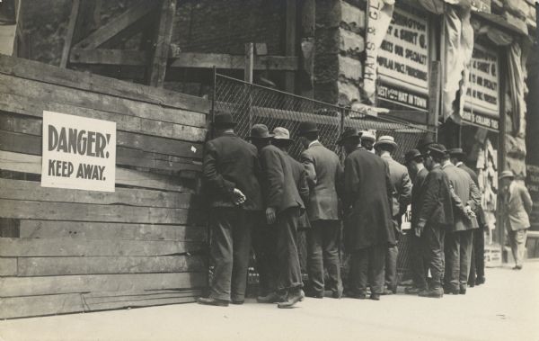 A group of men gather at a fence to observe construction.