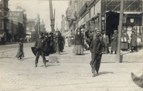 A street scene with pedestrians and police officer on a windy day in downtown Milwaukee.