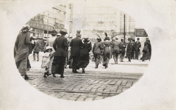 A line of pedestrians cross a busy street near a building with a sign for Gimbels Brothers.