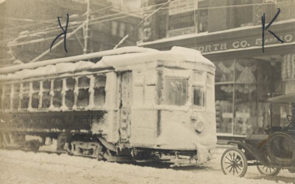 Winter scene with snow-covered street car. A sign on the storefront behind the street car reads: "[Wool]worth Co. 5 and 10".
